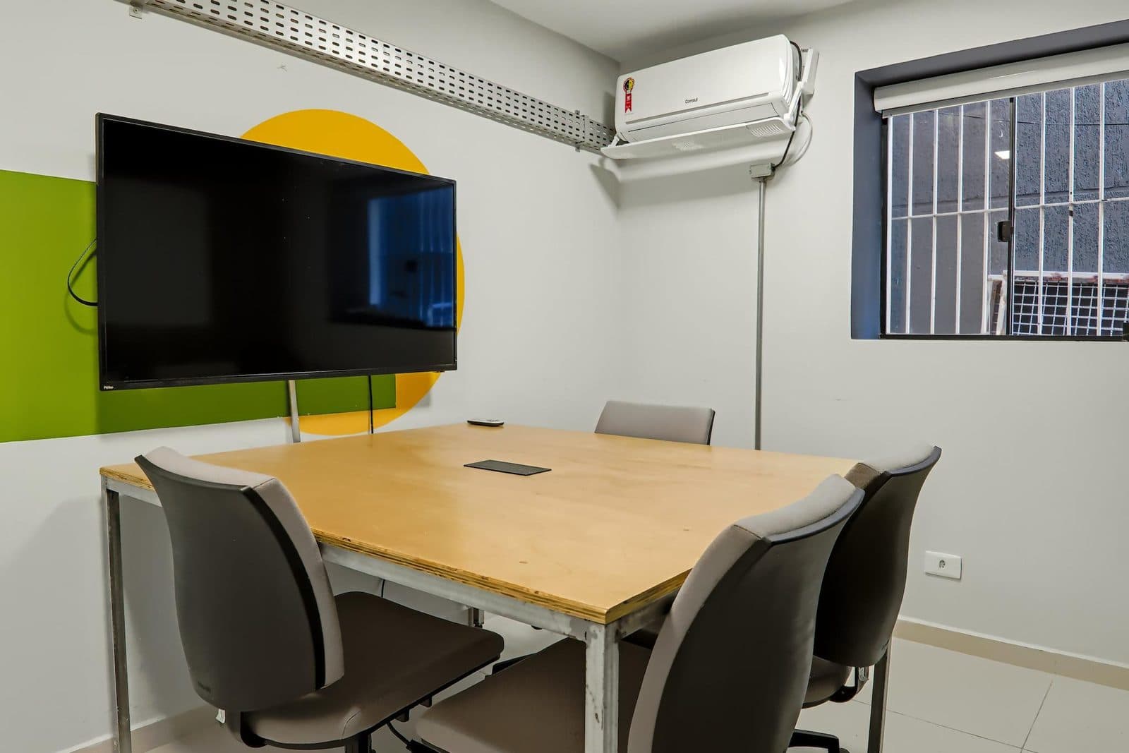 Sala de reunião equipada do Brains Batel, com mesa de madeira e televisor, em Curitiba