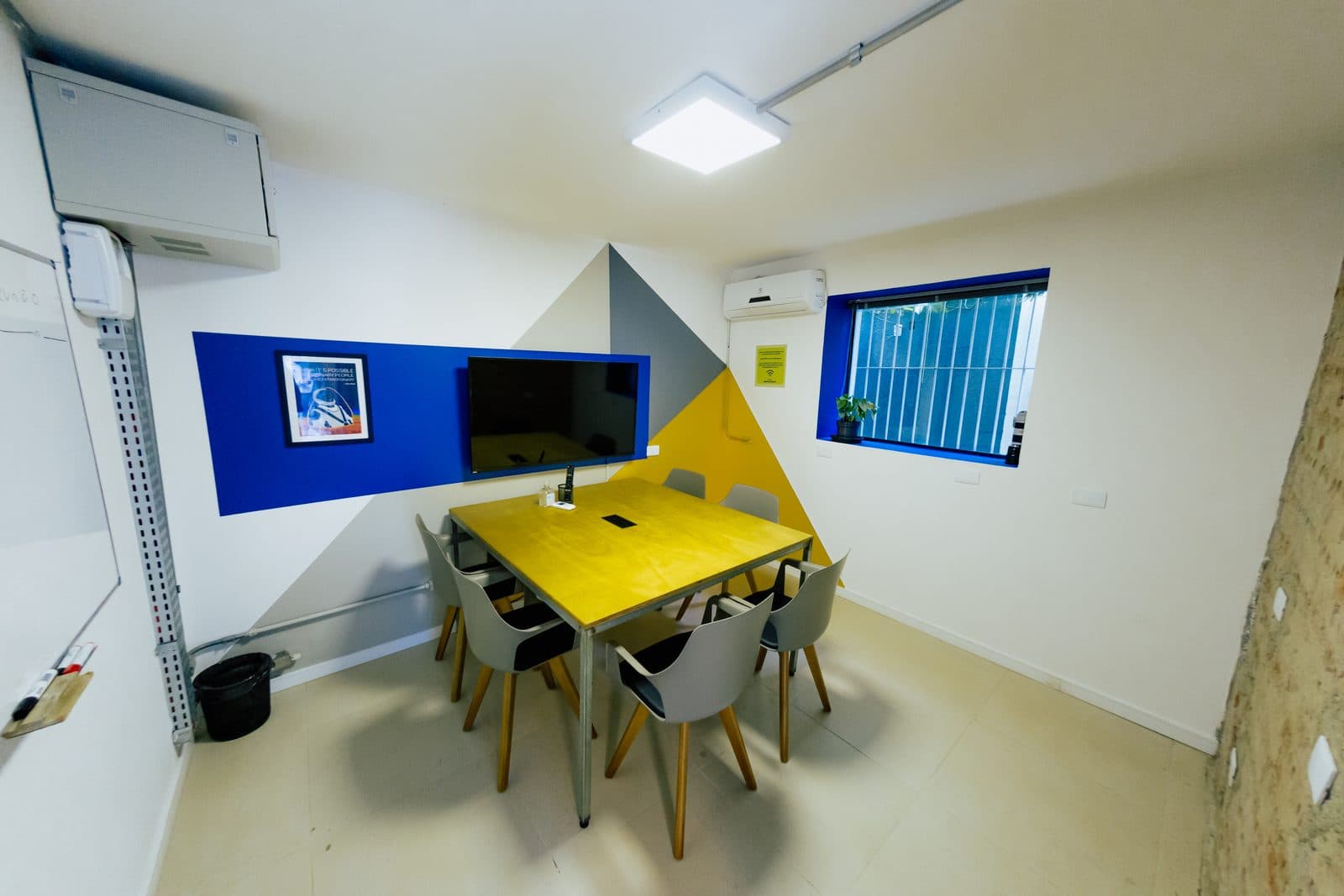 Sala de reunião do Brains Batel com mesa amarela e televisor, em Curitiba