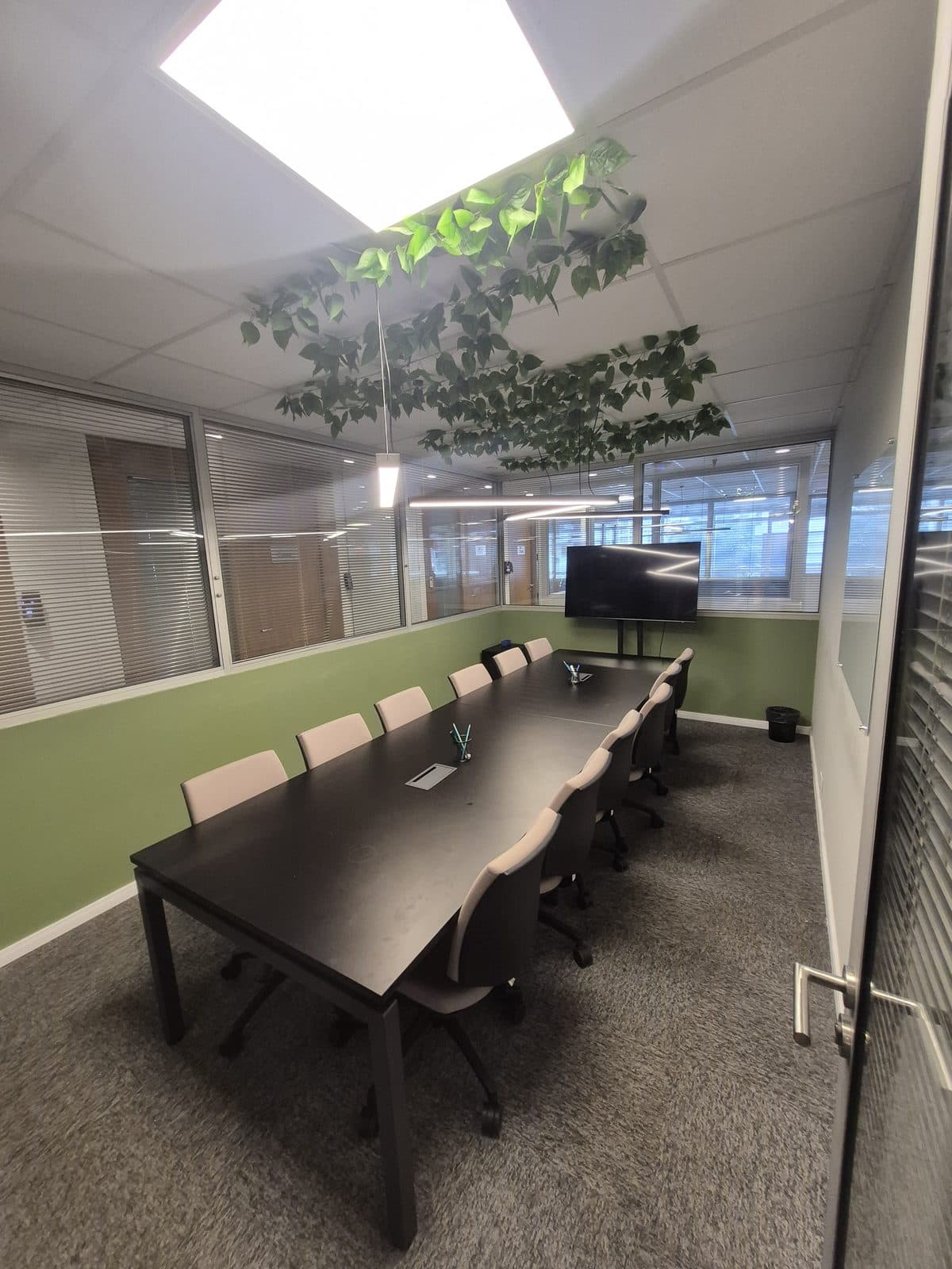 Sala de reunião do Brains Centro Cívico com parede verde e plantas suspensas, em Curitiba