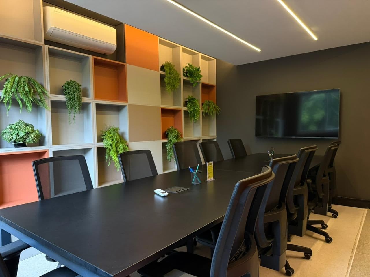 Sala de reunião do Brains Parque Barigui, com mesa longa para equipe, televisor e estante de nichos coloridos, em Curitiba
