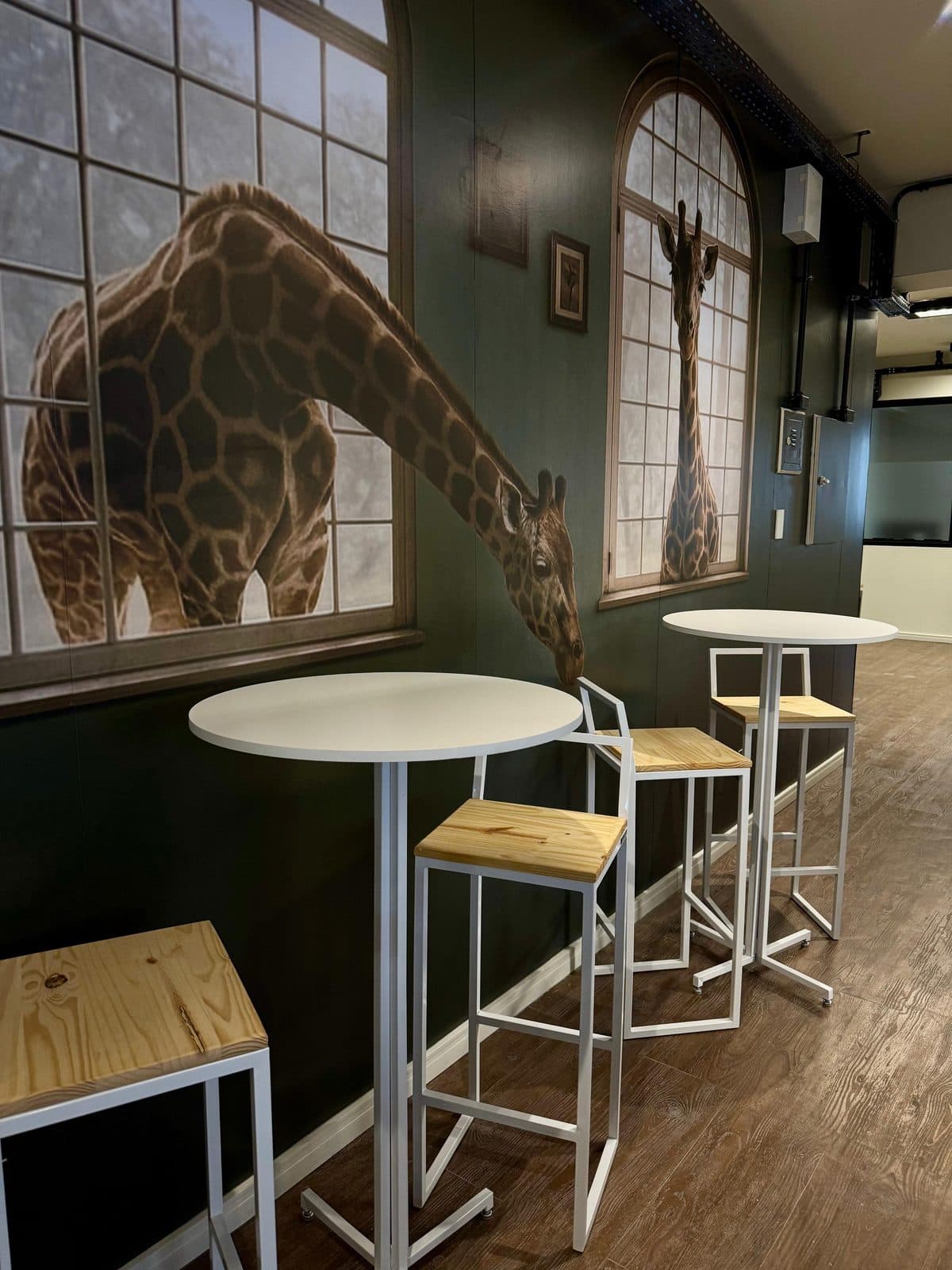 Área de convivência do Brains Praça do Japão, com mesas altas e mural ilustrado, em Curitiba
