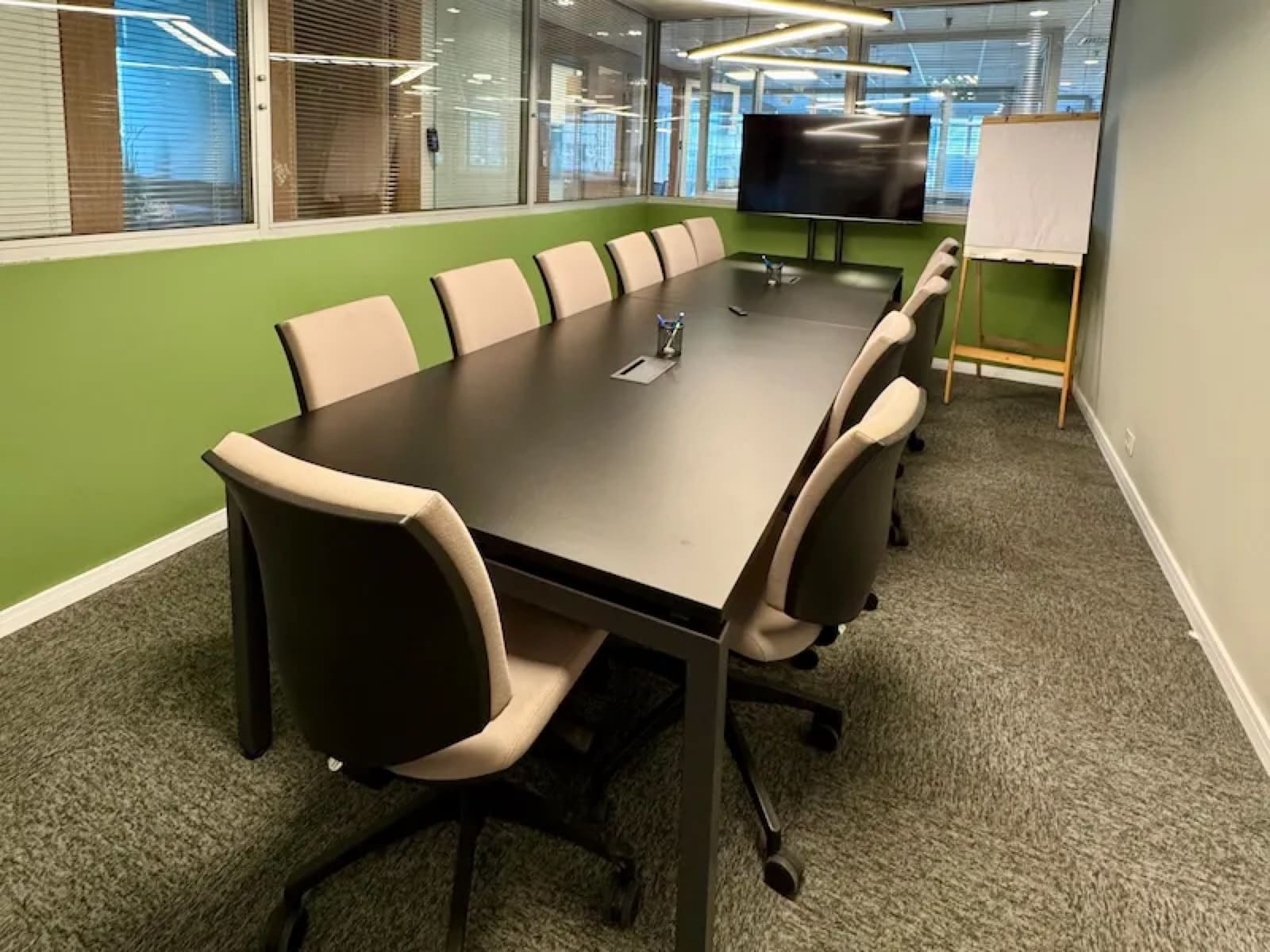 Sala de reunião da Brains Coworking Centro Cívico em Curitiba, com mesa para dez pessoas, televisão e flip chart