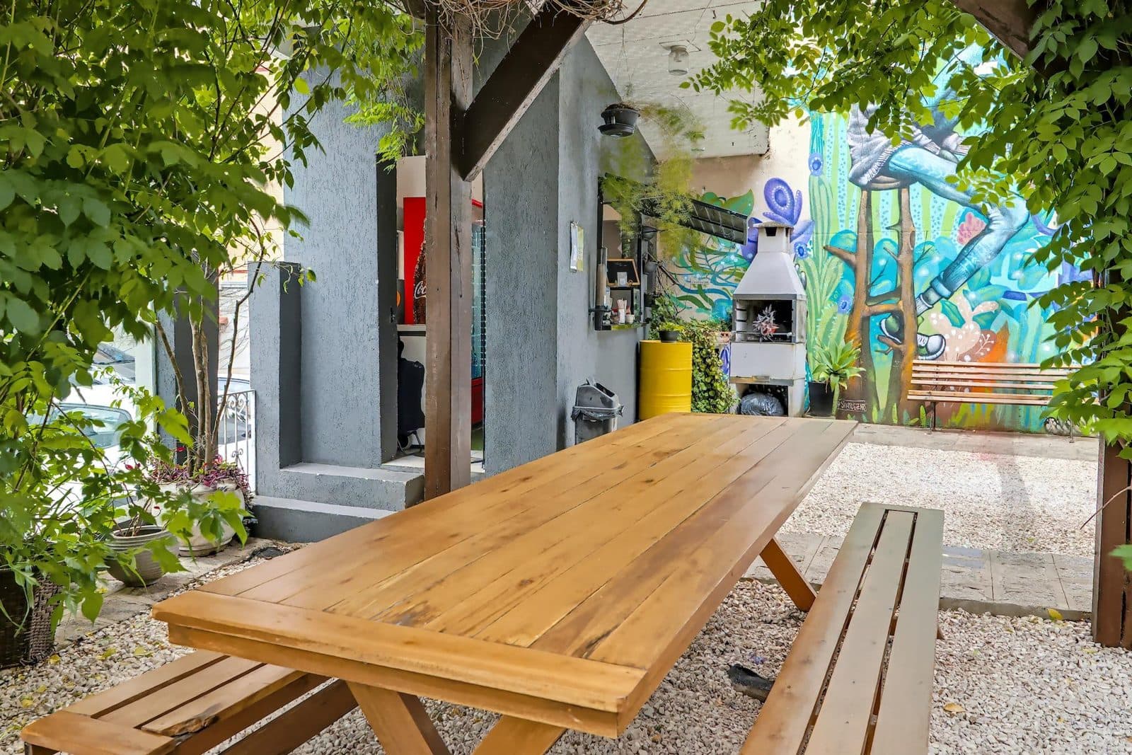 Área externa do Brains Batel com mesa de madeira sob o pergolado e mural grafitado, em Curitiba