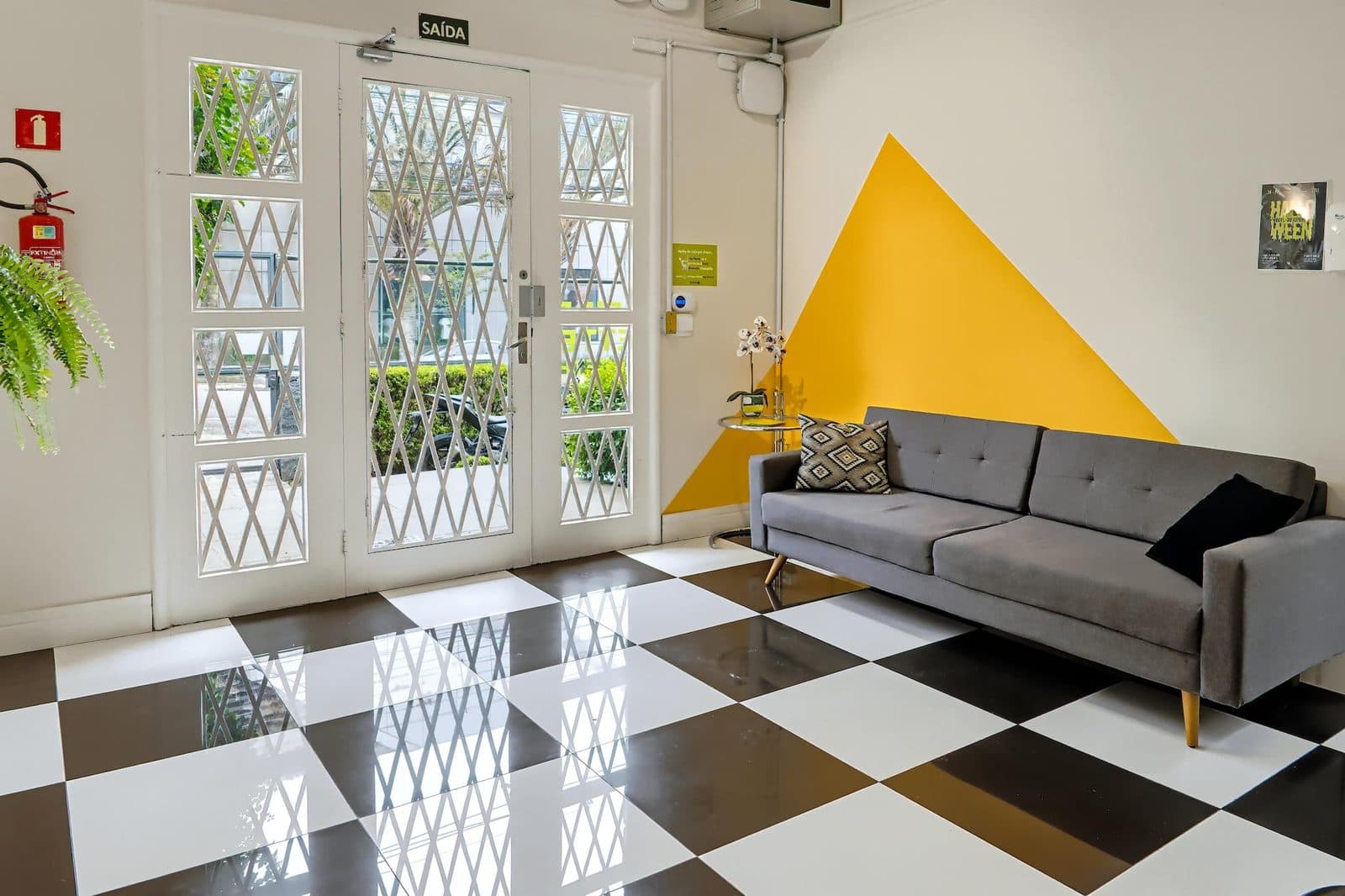 Sala de estar da Casa 2 do Brains Batel, com sofá e piso xadrez, em Curitiba