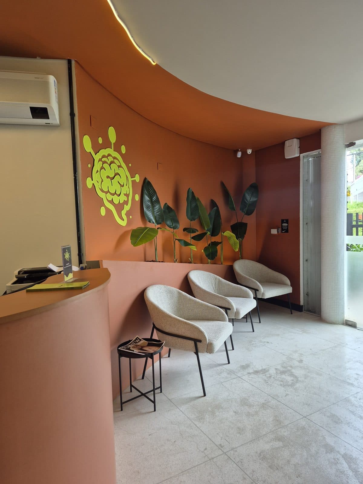Recepção do Brains Parque Barigui, com o cérebro da marca na parede terracota, em Curitiba